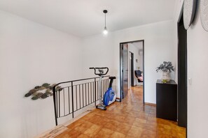 A hallway with a blue stationary bike, a black metal railing, and a tiled floor. - Holiday Home 'Villa Altura Beach' with Terrace & Wi-Fi (Altura)