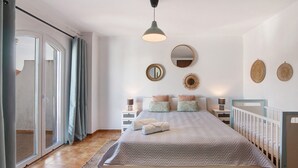 Une chambre à coucher comprenant un lit, des tables de chevet, une lampe suspendue, un miroir et une vue sur l’extérieur, accessible par une porte coulissante.