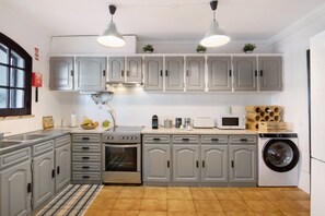 Una cocina con gabinetes grises, estufa, horno, microondas y lavadora.