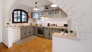 Une cuisine avec un arc en plein cintre blanc, des meubles gris, un lave-vaisselle, un four, un four à micro-ondes et des plantes en pot.