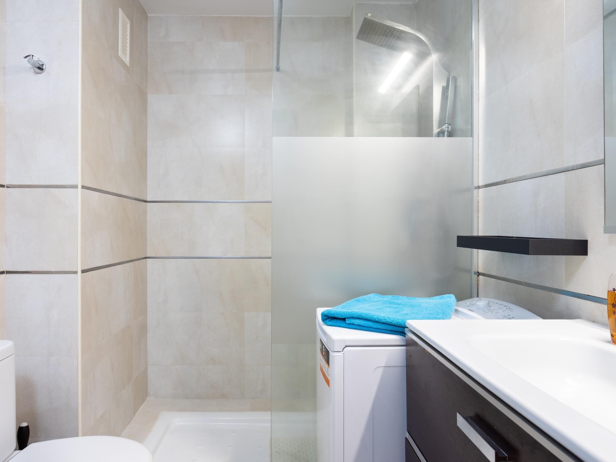 A modern bathroom with a glass shower enclosure, a white toilet, and a built-in washing machine.