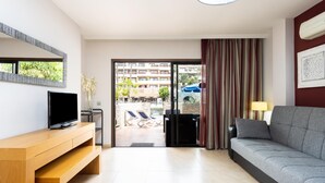 Sala de estar moderna com televisão de tela plana, painel de entretenimento em madeira, sofá cinza e vista para a área da piscina.
