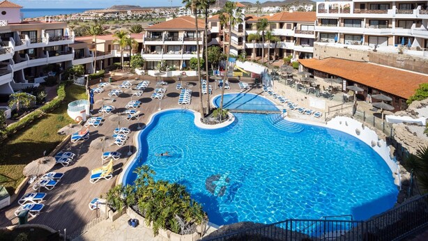 Um resort com uma piscina grande, várias varandas e vista para o oceano.