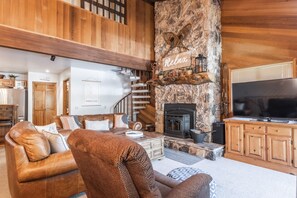 A cozy living room with a stone fireplace, wooden furniture, and a TV.