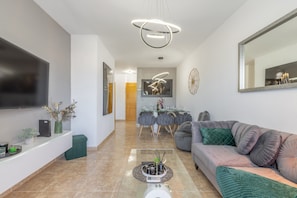 Ein modernes Wohnzimmer mit Fernseher, einer Couch, einem Couchtisch und einem Essbereich im Hintergrund.
