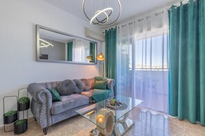 Un salon moderne avec un canapé, une table basse en verre, un miroir et une vue dégagée sur l’extérieur grâce à une grande fenêtre.