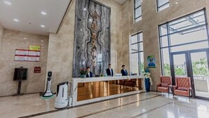 A hotel reception area with a marble reception desk, a large vertical sign with Chinese characters, and a seating area with two chairs. - Zhoushan Xinxiting Grand Hotel (Zhoushan)