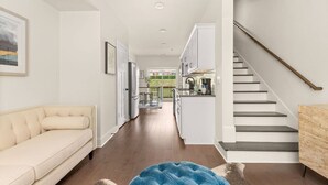 Ein modernes Interieur mit einer Couch, einem blauen Hocker, einer Treppe und einer Küchenzeile.