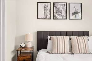 A bedroom with a bed, a nightstand with a lamp and clock, and three framed pictures on the wall.