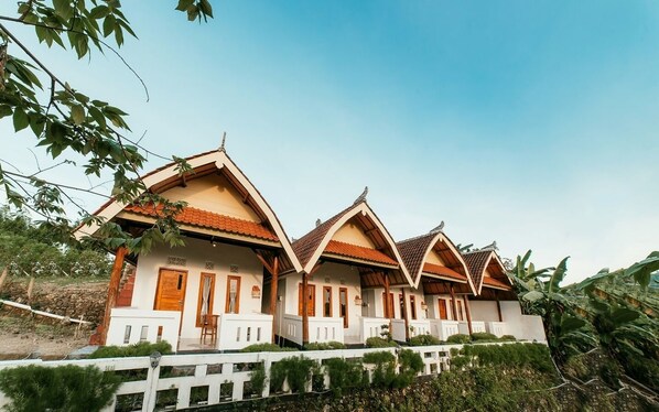 A row of traditional-style buildings with pitched roofs and wooden accents, surrounded by greenery. - Calista Cottage by best deals asia group (Penida Island)