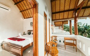 A bedroom with a bed, a wooden chair, a small table, and a balcony with a view of greenery. - Calista Cottage by best deals asia group (Penida Island)
