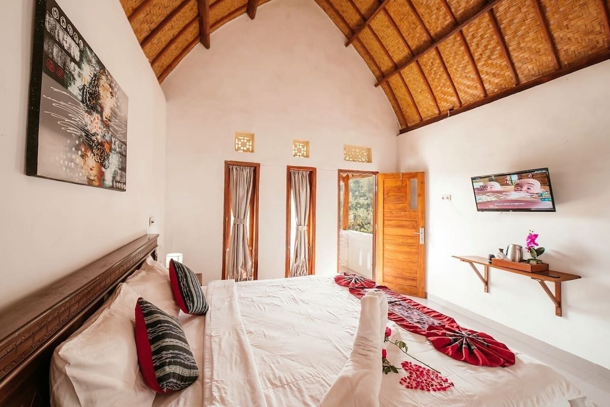 A bedroom with a large bed, a wooden headboard, a TV on the wall, and a window with curtains.