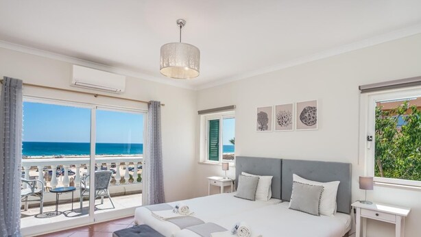 Una camera da letto con un grande letto, una panca, un comodino e vista sulla spiaggia.
