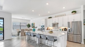 Une cuisine moderne avec des meubles blancs, un réfrigérateur en acier inoxydable et un grand îlot central doté de tabourets de bar.