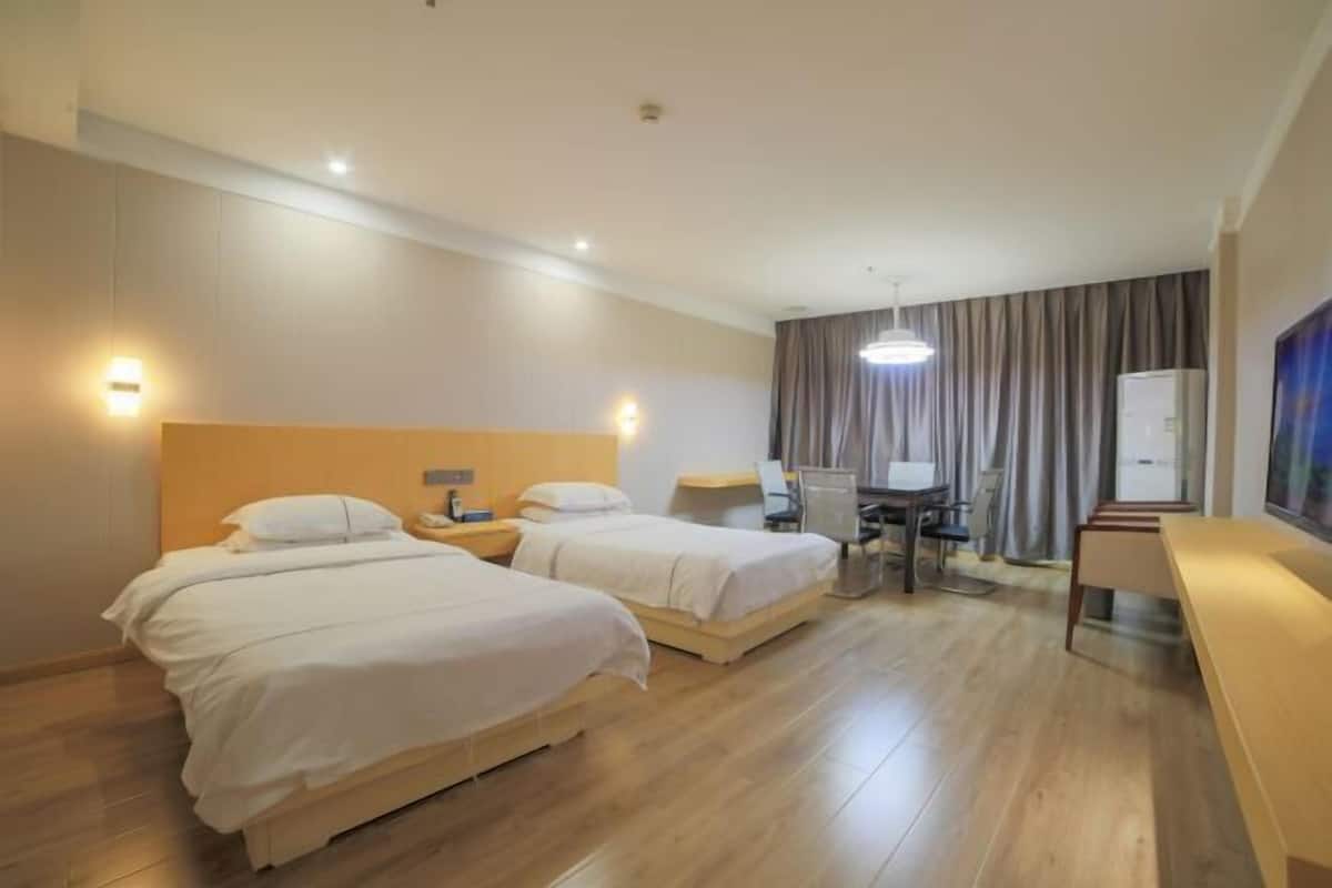 Una habitación de hotel con dos camas, un escritorio, una silla, un televisor y una lámpara en el techo.