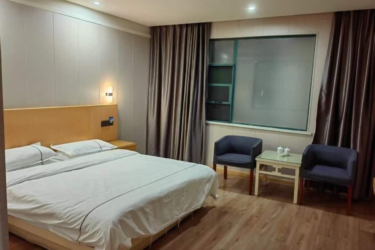Habitación de hotel con una cama grande, una mesita de noche, una pequeña mesa con dos sillas y un ventanal con cortinas.