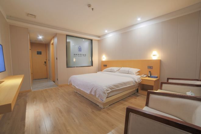 A hotel room with a bed, bedside table, lamp, and a view of the hallway.