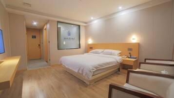 A hotel room with a bed, bedside table, lamp, and a view of the hallway.