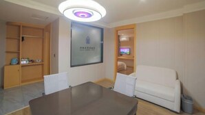 Una sala de conferencias con una mesa, sillas, un sofá, un televisor y una lámpara en el techo.
