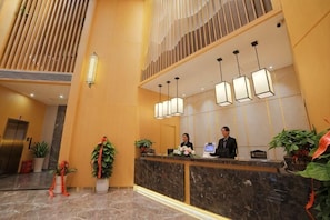 A hotel reception area with a marble counter, two receptionists, and modern pendant lighting.