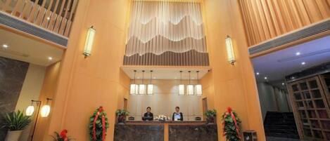 Zona de recepción de hotel con piso de mármol, mostrador de recepción y una escalera.