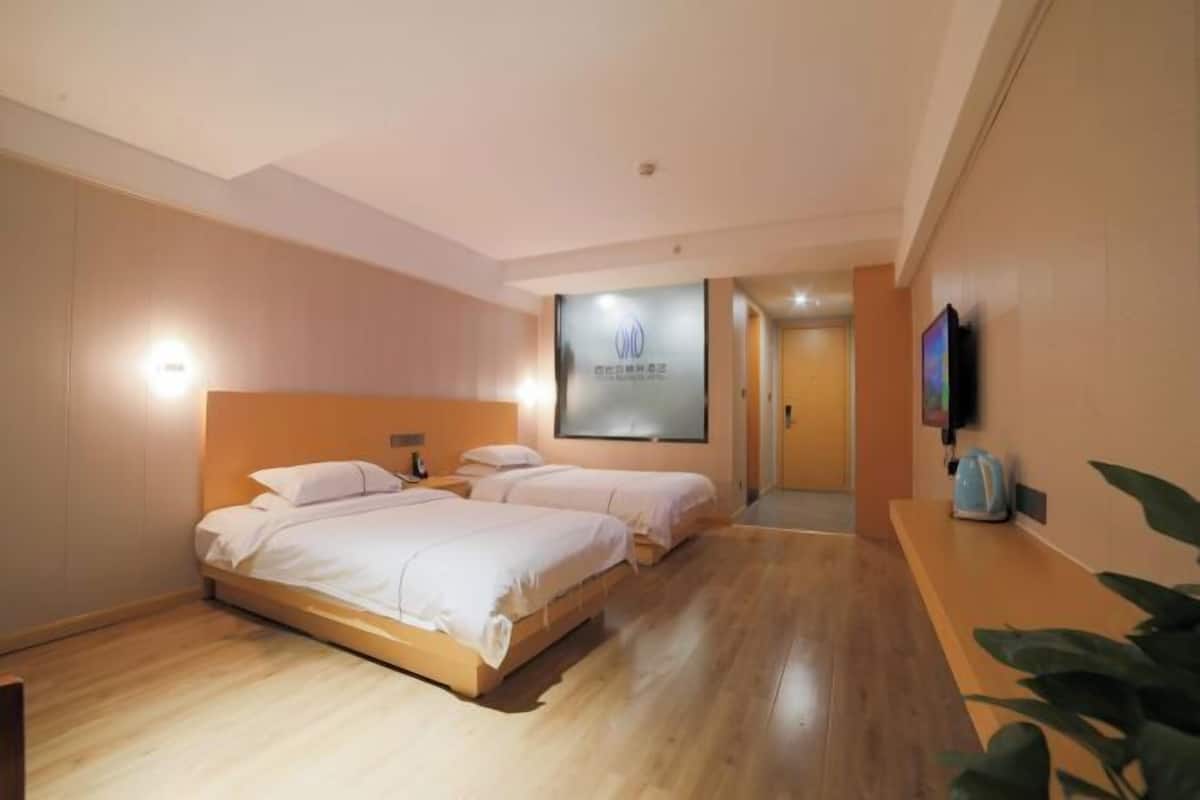 Habitación de hotel con dos camas, un televisor de pantalla plana montado en la pared y suelo de madera.