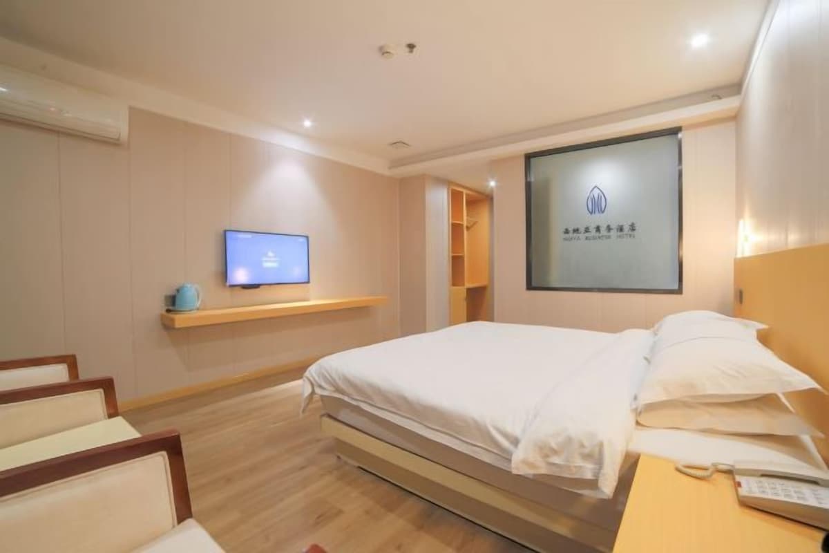 A hotel room with a bed, a TV, a desk with a phone, and a wall-mounted shelf.