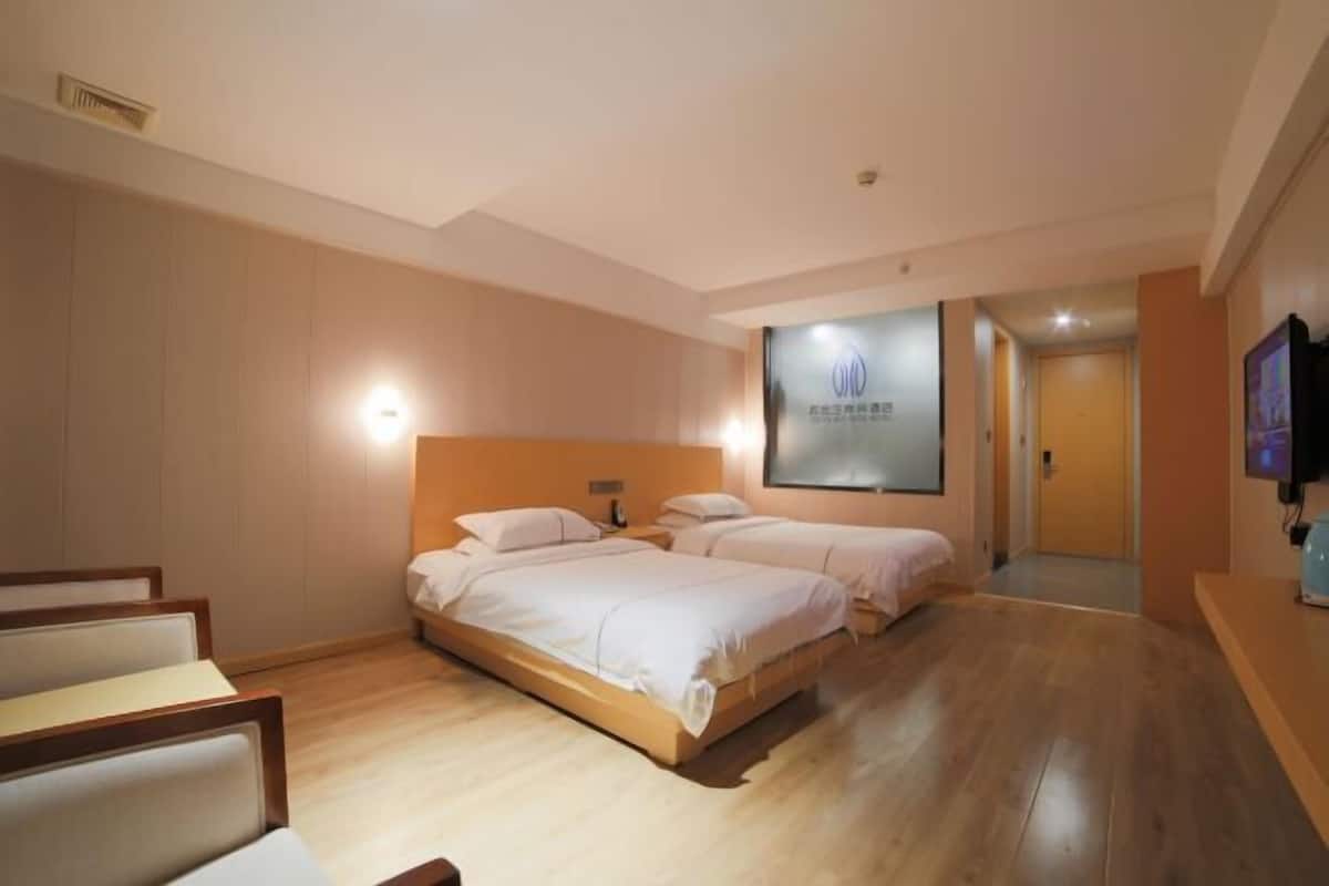 Habitación de hotel con dos camas, piso de madera, cabecera con lámpara y televisión de pantalla plana, además de una obra de arte colgada en la pared.