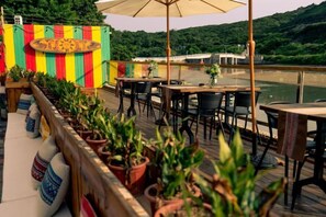 An outdoor terrace with tables and chairs, potted plants, and a view of a body of water. - Time and Sea Inn (Shenzhen)