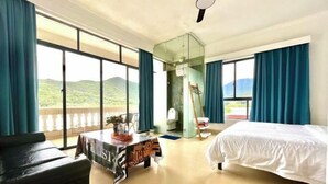 A hotel room with a bed, a table with a magazine, a chair, a glass partition, and a view of the outdoors. - Time and Sea Inn (Shenzhen)