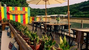 An outdoor dining area with wooden tables and chairs, surrounded by potted plants and a colorful striped wall. - Time and Sea Inn (Shenzhen)