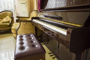 A piano, a cushioned bench, and a patterned armchair in a room with a tiled floor. - Time and Sea Inn (Shenzhen)