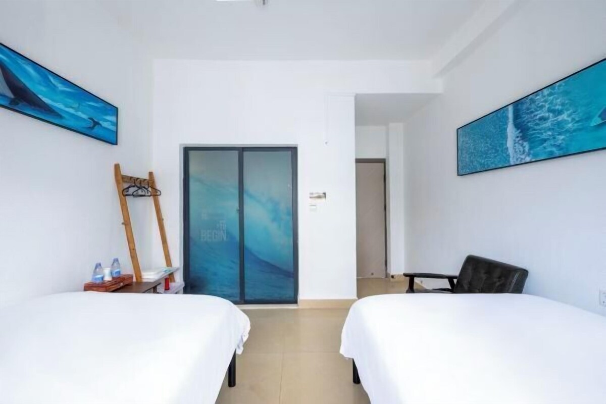 A hotel room with two beds, a wooden chair, a table, and a door with a glass panel.
