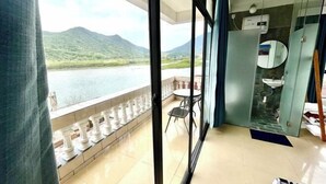 A balcony with a view of a lake and mountains, a glass partition, a round mirror, and a sink. - Time and Sea Inn (Shenzhen)