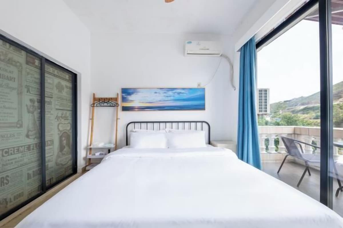 A hotel room with a bed, a painting, a window, and a balcony with a chair.