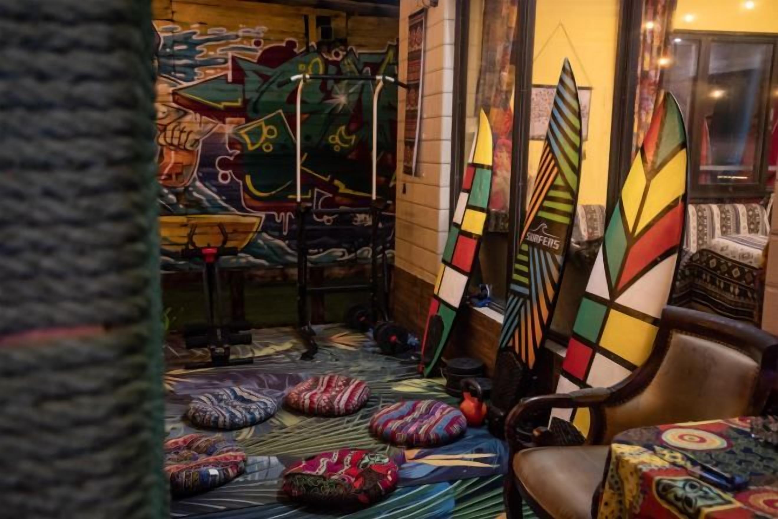 A room with colorful artwork on the walls, a bed with a patterned bedspread, and a chair with a decorative cushion.