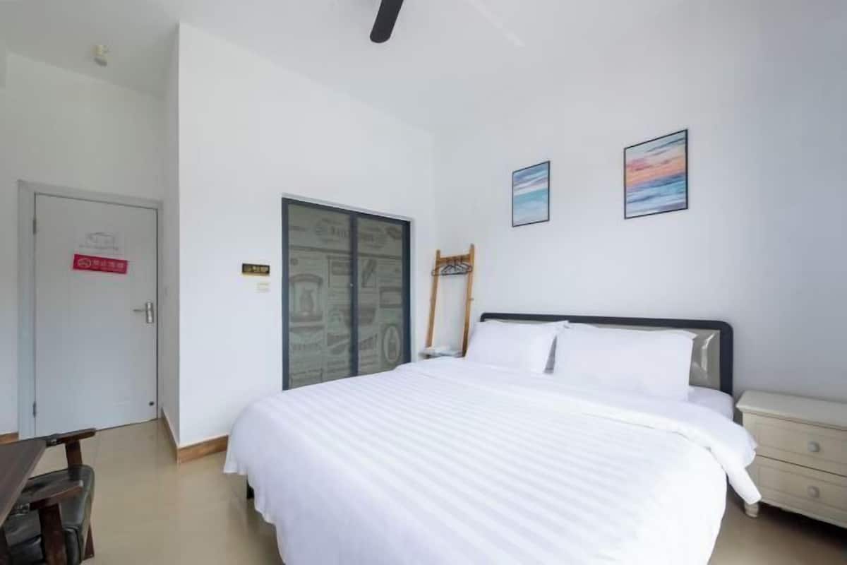 A hotel room with a bed, a desk, and a chair. There is a door with a sign, a window, and a wall with two framed pictures.