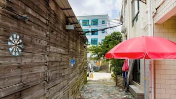 Un estrecho callejón con un muro de madera, un paraguas rojo y un edificio con suelo de baldosas al fondo.