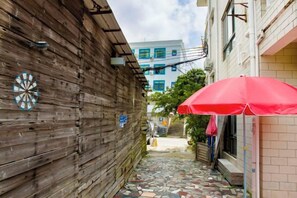 A narrow alleyway with a wooden wall, a red umbrella, and a building with a tiled floor in the background.
