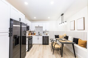 A modern kitchen with white cabinets, stainless steel appliances, and a dining area with a bench and table.
