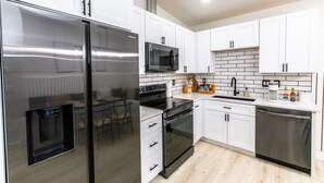 Een moderne keuken met witte kasten, roestvrijstalen apparatuur en een betegelde spatwand.