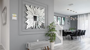 Un salon moderne avec un mur gris, une grande œuvre d’art abstraite, un banc gris, une plante en pot et un escalier menant à un espace repas avec une table et des chaises.