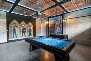 A pool table with a blue felt surface, a billiards cue, and balls, in a room with a decorative ceiling and a large poster of a castle.