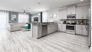 Une cuisine moderne avec des meubles gris, un îlot central, des appareils en acier inoxydable et un coin repas agrémenté d’une chaise verte.