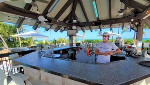 A bar area with a counter, bar stools, and a person standing behind the counter.