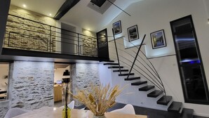 A modern interior with a stone wall, a staircase, and a dining area with a vase of dried plants.