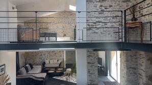 A multi-level interior with a stone wall, a balcony with a metal railing, and a seating area with sofas and a coffee table.