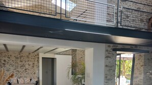 A spacious living area with a high ceiling, a dining table with chairs, a sofa, and a staircase with a railing.