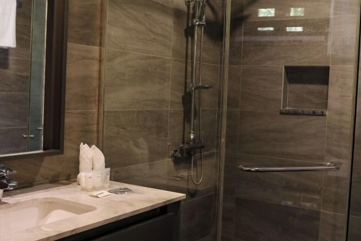 Un baño moderno con ducha envuelta en cristal, lavamanos con espejo y un perchero para toallas.