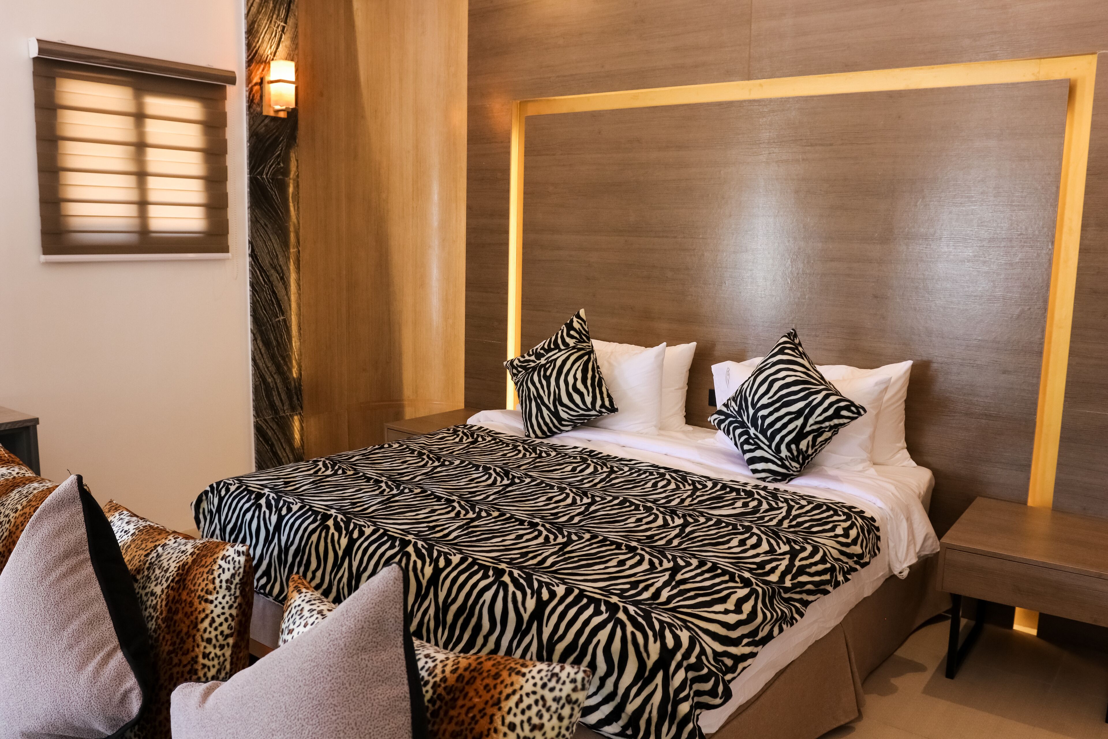 A hotel room with a zebra-patterned bedspread, a wooden headboard, and a nightstand with a lamp.